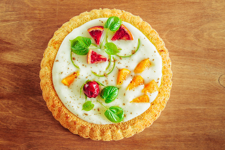 gentle magnificent biscuit with vegetable vanilla cream decorated with fruit, a bud of a rose and young leaves on a wooden table, the top view, a close upの写真素材