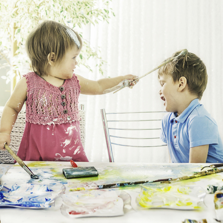 the little girl holds in hand art brushes and one of them draws on the head of the little boy who laughs, close-upの写真素材