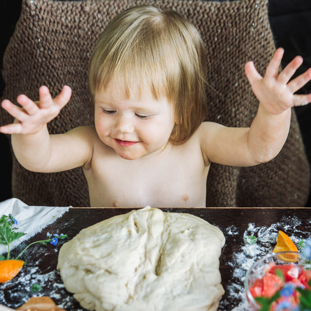 The baby claps hands according to the test against the background of a wooden table and a set of products for preparation of pie with grapefruit and carrots, close upの写真素材