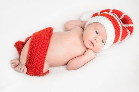 Newborn baby 2 weeks old in red santa claus cap and scarf lies on white background