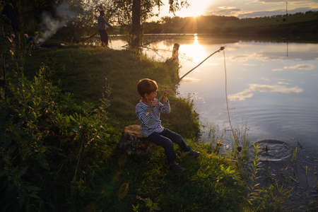 a boy fishing on the shores of a village lake at sunset, close upの写真素材