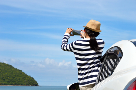 Happy woman taking photos to the sea with smartphone camera on carの写真素材