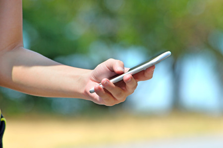 Woman hand holding smartphone against nature backgroundの写真素材