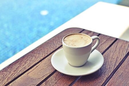 Morning cup of coffee on wooden table with pool backgroundの写真素材