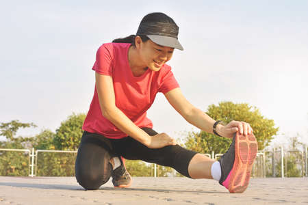 Young fitness woman runner stretching legs before run on park