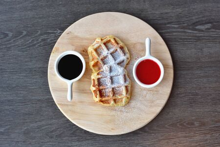 Home made Belgian waffles served with strawberry sauce and chocolate sauce over a wooden  board.