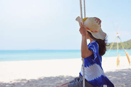 Woman sitting on rope swing at tropical beachの写真素材