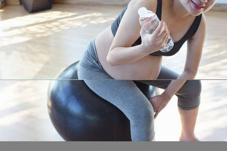 Pregnant woman resting on a yoga ball holding a water bottleの写真素材