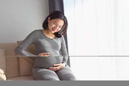Happy pregnant woman smiling  while sitting on couch at homeの写真素材