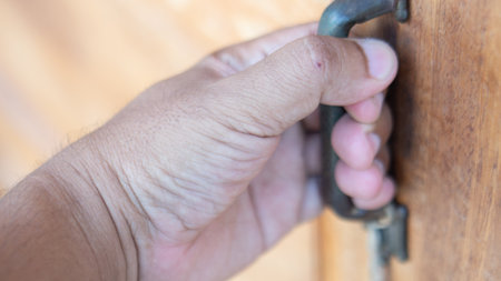 A close-up image of a hand gripping the handle of a wooden door, representing themes of access, entry, and personal connection to everyday spaces.の写真素材