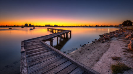A stunning sunset landscape featuring a wooden pier stretching out over calm waters, with a vibrant sky and distant city skyline. The tranquil scene evokes peace and relaxation.の素材