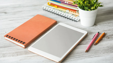 Tablet with stylus beside a stack of notebooks and gel pens on a deskの素材