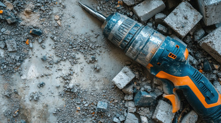 Electric hammer drill lying next to concrete blocks with dust and debrisの素材