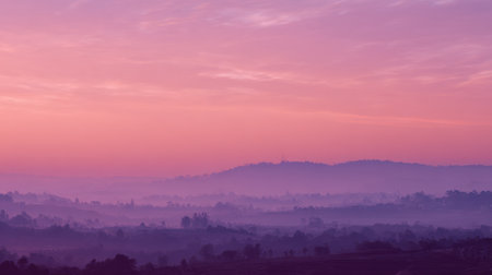 This captivating landscape captures the serene beauty of dawn, showcasing rolling hills enveloped in mist and soft pastel colors that evoke peace and calm.の素材