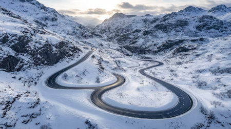 An aerial view captures a winding road through stunning snow-covered mountains, showcasing the serene beauty of winter nature at sunrise. Perfect for travel and adventure themes.の素材