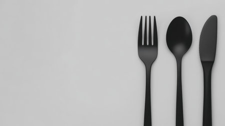This image features an elegant black cutlery set placed on a soft gray background, ideal for showcasing minimalist dining styles and food presentation.の素材