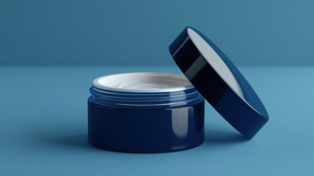 A modern blue cosmetic container with an open lid, revealing a creamy interior on a soft blue background. Perfect for skincare and beauty product applications.の素材