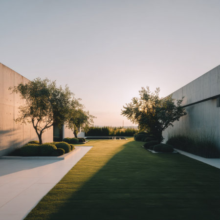 A tranquil outdoor landscape featuring lush green grass, elegant trees, and minimalist concrete walls set against a soft sunset sky, capturing serene beauty.の素材
