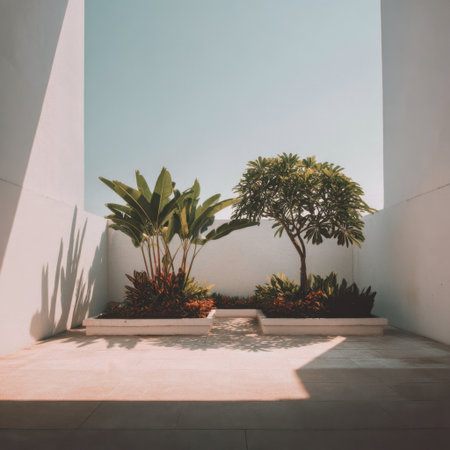 This image captures a tranquil modern courtyard filled with rich green plants, warm stone flooring, and bright sunlight, creating a serene and inviting atmosphere.の素材