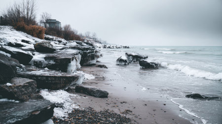 A tranquil winter landscape showcases a rocky beach with icy formations and gentle waves under a grey sky, evoking a sense of peace and solitude in nature.の素材