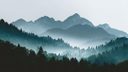 Stunning view of a misty mountain landscape featuring lush green forests and majestic peaks, creating a tranquil and serene atmosphere in early morning light.の素材