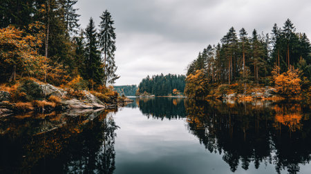 Experience the beauty of an autumn landscape featuring vibrant foliage and calm waters, reflecting a serene forest and cloudy sky in a tranquil setting.の素材