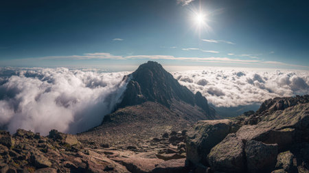 A stunning mountain peak rises majestically above a sea of clouds under brilliant sunlight. The rocky foreground invites exploration of this serene, breathtaking landscape.の素材