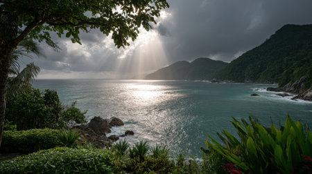 A breathtaking coastal view showcasing sunlight piercing through clouds over gentle ocean waves, surrounded by vibrant greenery and rocky terrain, evoking peace.の素材
