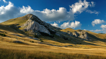 A stunning view of rolling hills adorned with dramatic rock formations under a vibrant blue sky filled with fluffy clouds, offering a peaceful natural scene.の素材
