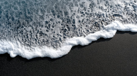 View of ocean waves gently crashing on dark sand beach. The white foam creates intricate patterns, reflecting the beauty of nature and the serene atmosphere.の素材