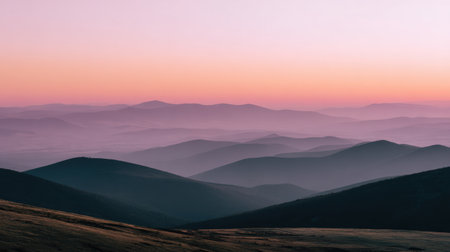 A stunning view of rolling hills at dawn, showcasing soft pastel colors in the sky. The tranquil landscape features layered mountains fading into the horizon.の素材