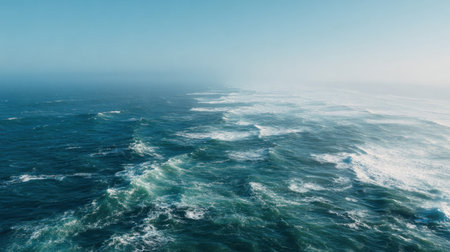 Experience the calming beauty of the ocean with gentle waves rolling towards the horizon under a clear sky, enhanced by a soft mist, creating a tranquil coastal scene.の素材