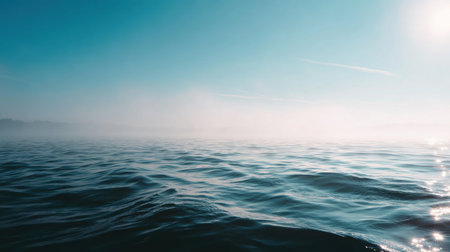 Experience the peaceful beauty of ocean waters under a bright blue sky, where gentle waves create a tranquil scene, enhanced by soft fog on the horizon.の素材