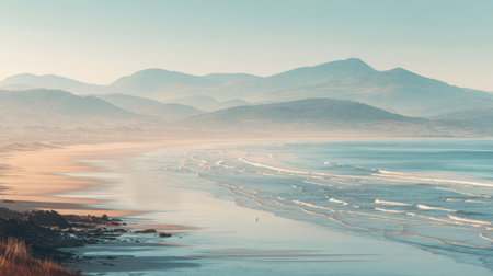 Breathtaking coastal scene featuring gentle waves lapping against a sandy shore, set against misty mountains in the background, perfect for nature lovers and travelers.の素材