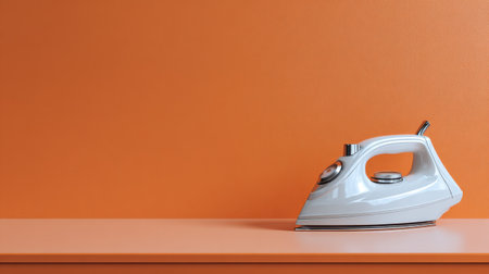 A sleek steam iron is featured on a pastel orange tabletop with a matching wall. The image emphasizes minimalist design and modern home appliances for stylish living spaces.の素材