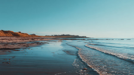 A tranquil coastal scene featuring gentle waves breaking on the sandy shore under a vast blue sky, perfect for evoking peace and serenity in any project.の素材