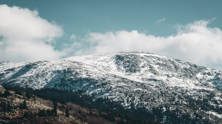 Captivating view of a snow-covered mountain range under a clear blue sky adorned with fluffy clouds. Perfect for showcasing the beauty of winter landscapes and nature.の素材