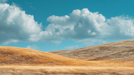 A breathtaking view of rolling golden hills contrasted by a stunning blue sky filled with white clouds, inviting peace and inspiration for outdoor enthusiasts.の素材