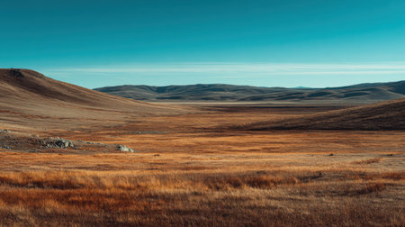 Captured in warm lighting, this stunning landscape showcases vast expanses of dry grassland and gentle hills under a clear blue sky, offering a tranquil escape into nature.の素材