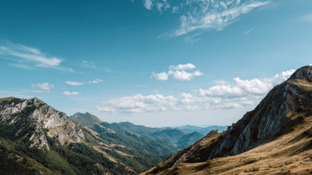 Stunning mountain landscape showcasing a vast view with lush green hills, a clear blue sky, and soft white clouds. Perfect for travel and nature enthusiasts.の素材