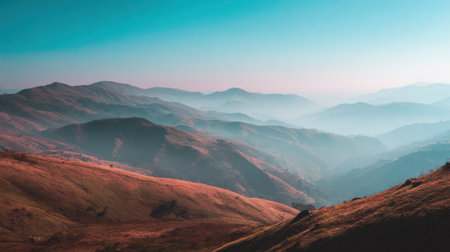 A stunning view of rolling hills and misty mountains under a blue sky at dawn. The vibrant pink and orange hues create a peaceful and serene atmosphere, perfect for nature lovers.の素材