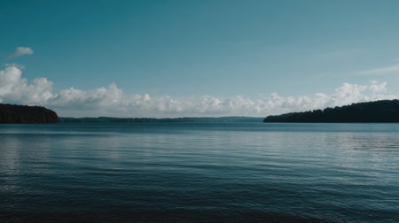 A calming view of a lake surrounded by lush greenery and fluffy white clouds. The tranquil waters reflect the blue sky, creating a peaceful natural escape.の素材