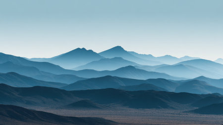 An expansive view of a serene mountain range showcases layered peaks and gentle hills bathed in soft blue tones. The clear sky enhances the tranquil atmosphere.の素材
