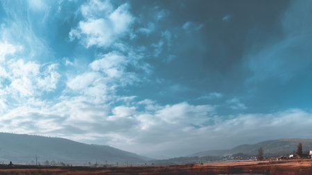 This breathtaking landscape features a vast sky filled with soft clouds, rolling hills, and a tranquil field, encapsulating the serenity of a peaceful rural environment.の素材