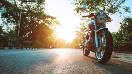 A stylish vintage motorcycle stands parked on an empty road at sunset, surrounded by lush trees and bathed in warm sunlight, inviting adventure and exploration.の素材