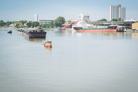 A small tug boat towing a large sand tanker in the Chao Phraya River, bangkok, thailand.の写真素材