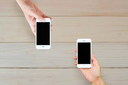 Woman hand holding and using mobile,cell phone,smart phone with isolated screen on wooden table or wooden floor for background.の写真素材