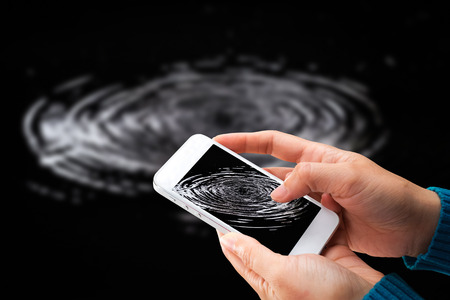 Woman hand holding and using mobile,cell phone,smart phone with isolated screen with blurred water ripples from a drop of water in the dark.の写真素材