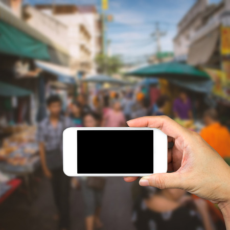 Woman hand holding and using mobile,cell phone,smart phone with isolated screen with blur image of people for background.の写真素材