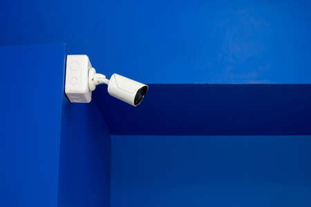 CCTV camera on blue concrete wall to record private or public spaces White Close Circuit Television is working by recording an event with red indicator light for the duration of its operationの写真素材